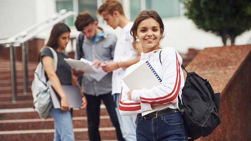 Cute teen girl. Group of young students in casual clothes near university at daytime.